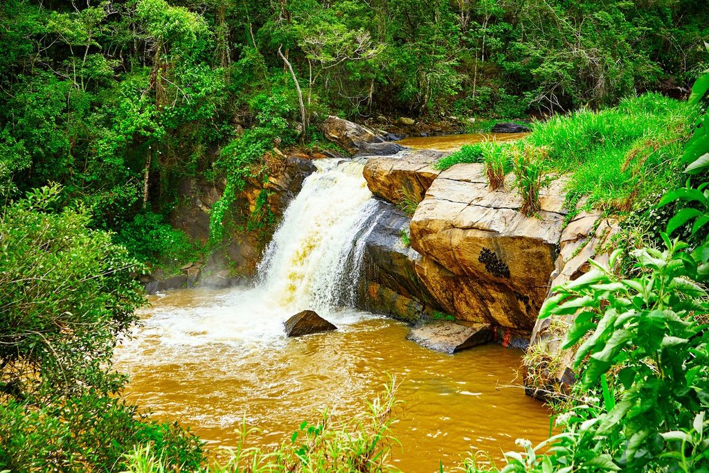Cachoeira das Andorinhas, em Monte Alegre do Sul, com água barrenta descendo entre grandes pedras e mata dos dois lados
