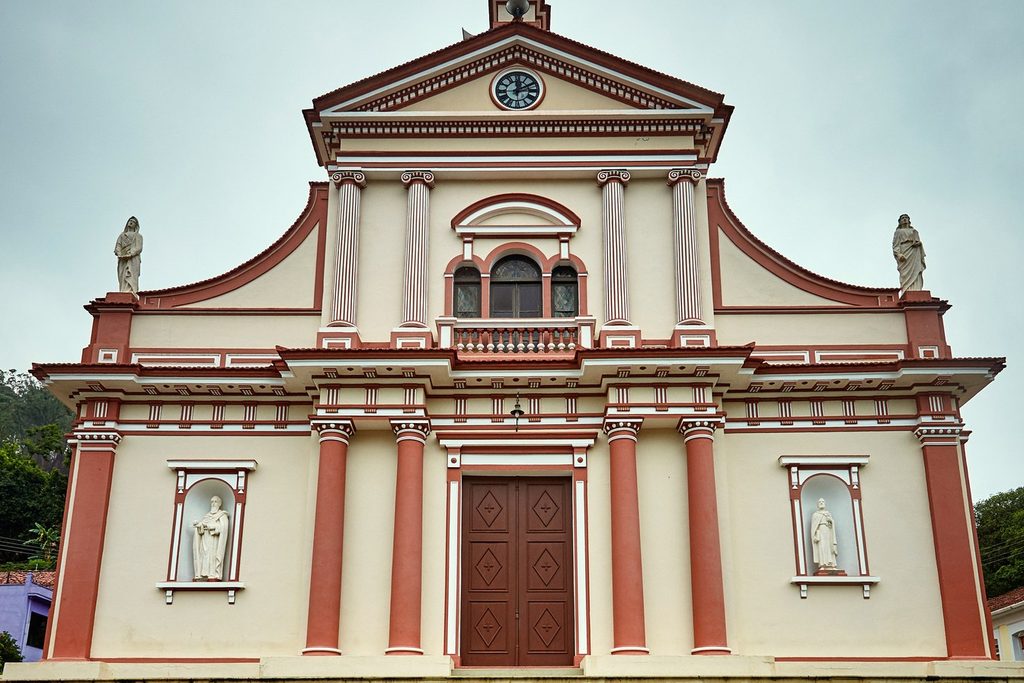 Fachada rosa e branca do Santuário do Senhor Bom Jesus, com relógio, colunas e estátuas de santos em nichos