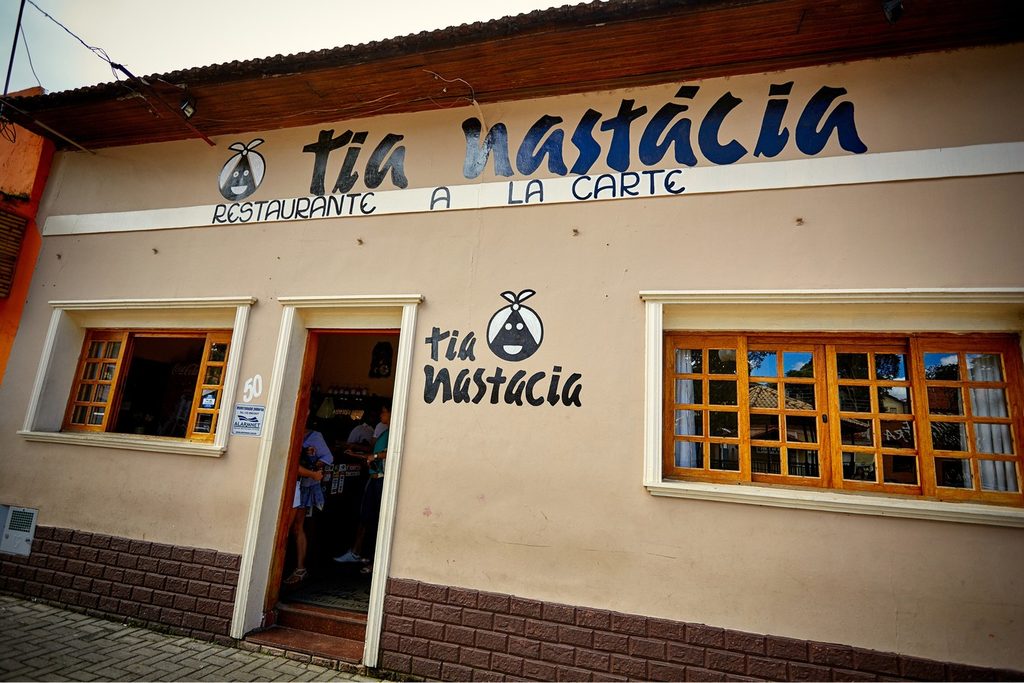 Fachada branca do restaurante Tia Nastácia, com janelas de madeira e letreiro azul