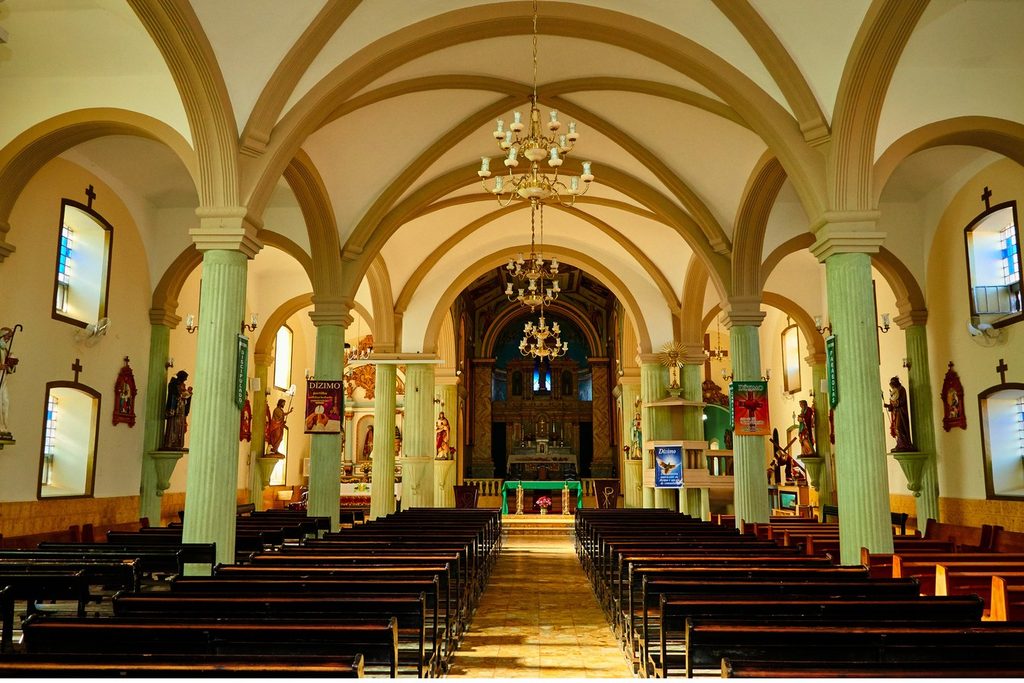 Interior da igreja com arcos, colunas verdes, lustres e o altar entalhado ao fundo