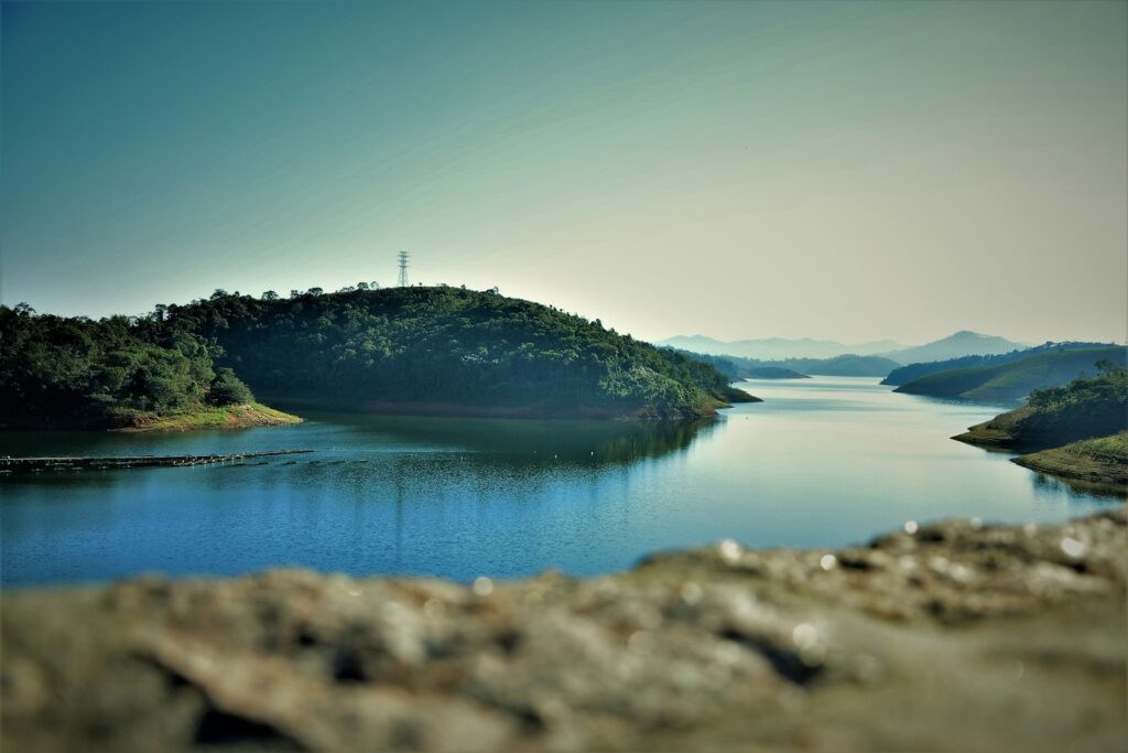 Represa de Paraibuna entre morros cobertos de mata, com ilhas e serras azuladas no horizonte