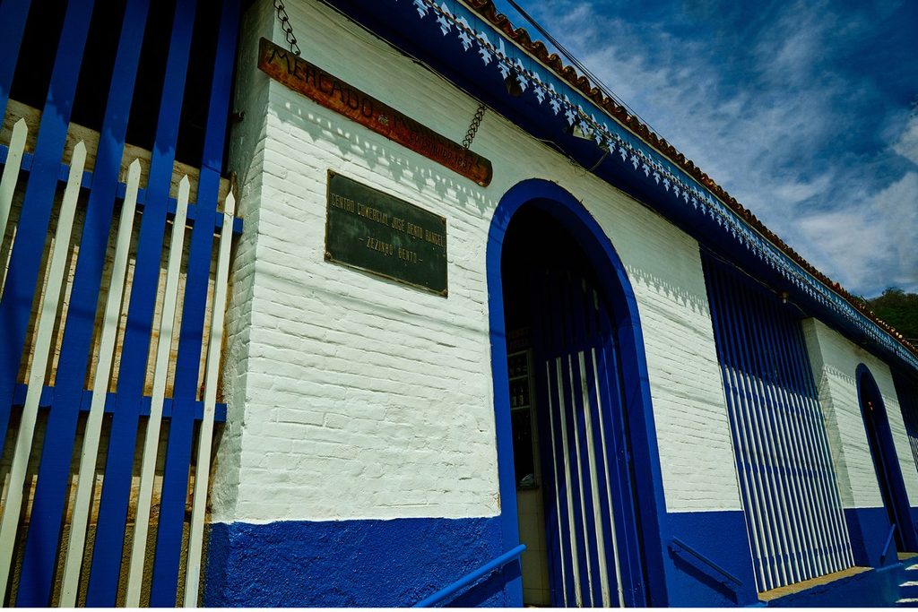 Fachada branca e azul do Mercado Municipal de Paraibuna, com portões de grade e porta em arco