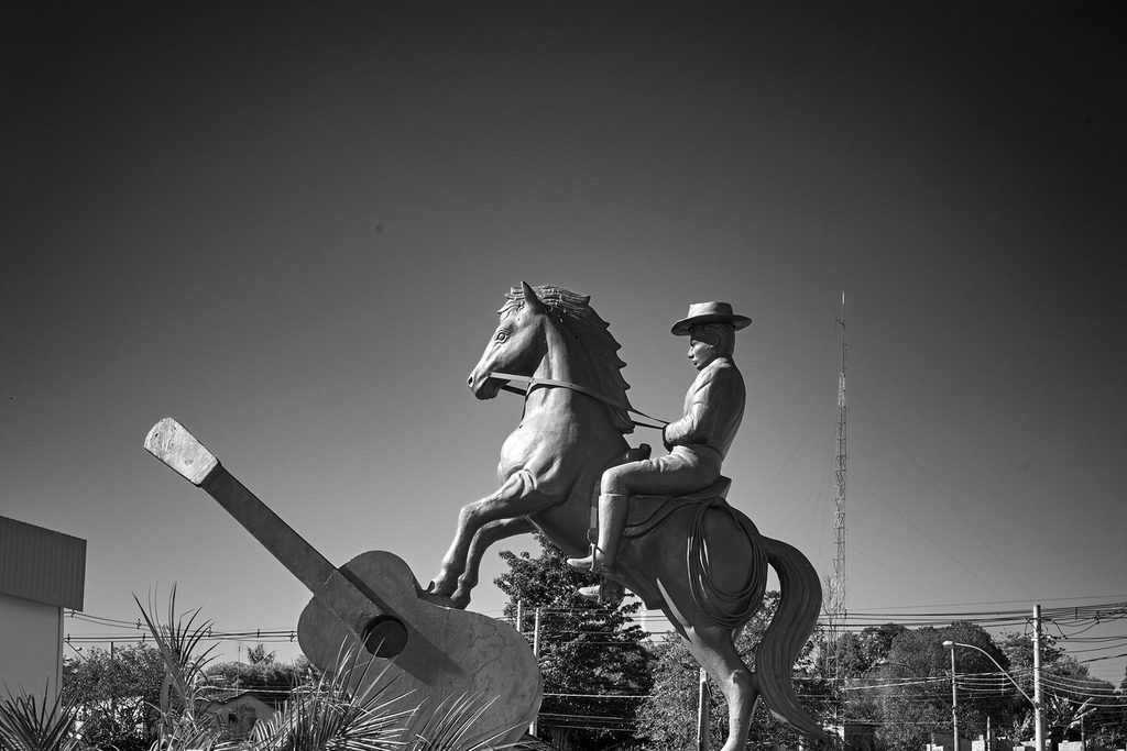 Estátua de cavaleiro com chapéu sobre um cavalo empinado ao lado de um violão gigante, o Monumento ao Ferreirinha