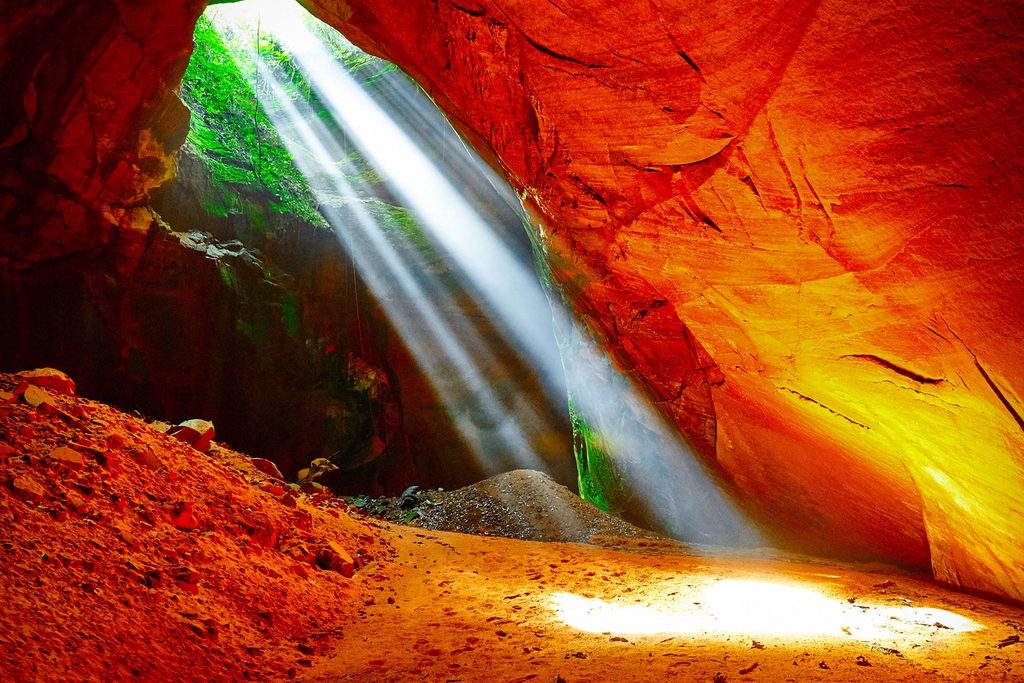 Raios de sol entrando pela abertura da caverna Buraco da Odete, em Pedregulho, e iluminando as paredes de pedra avermelhada