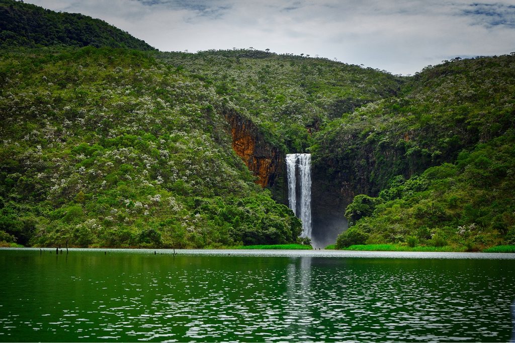 Cachoeira do Estreito caindo numa fenda entre morros verdes até o lago, em Pedregulho