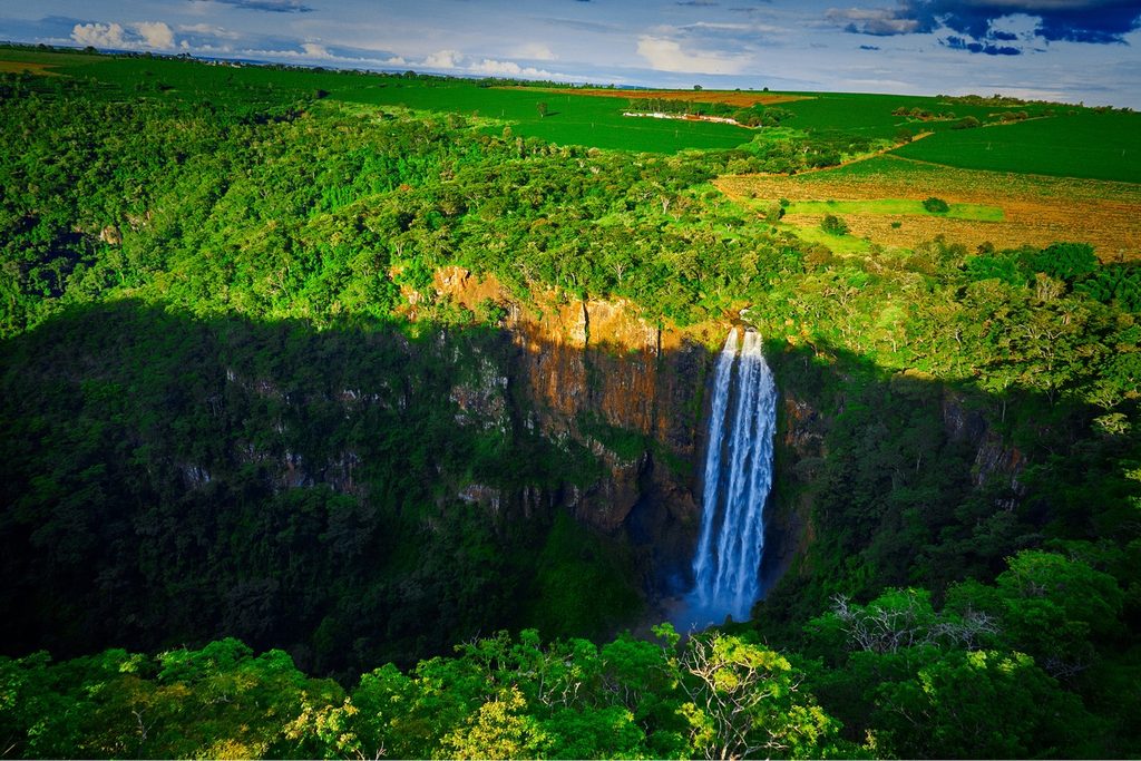 Cachoeira alta e fina caindo de um paredão de pedra no meio do cânion coberto de mata, no Parque Estadual Furnas do Bom Jesus