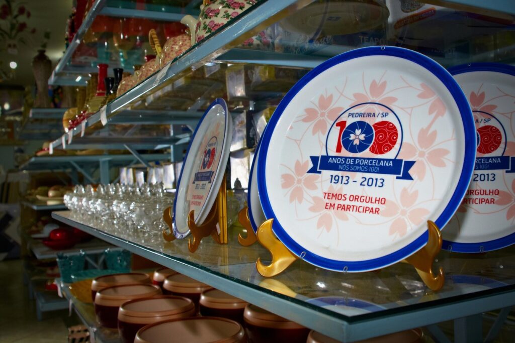 Prato comemorativo de porcelana branca e azul com a inscrição 100 anos de porcelana 1913-2013, exposto numa prateleira de loja
