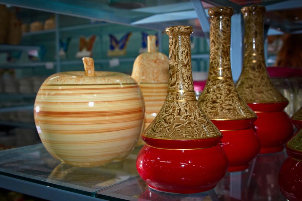 Prateleiras de vidro com potes de porcelana listrados e vasos vermelhos e dourados numa loja de Pedreira