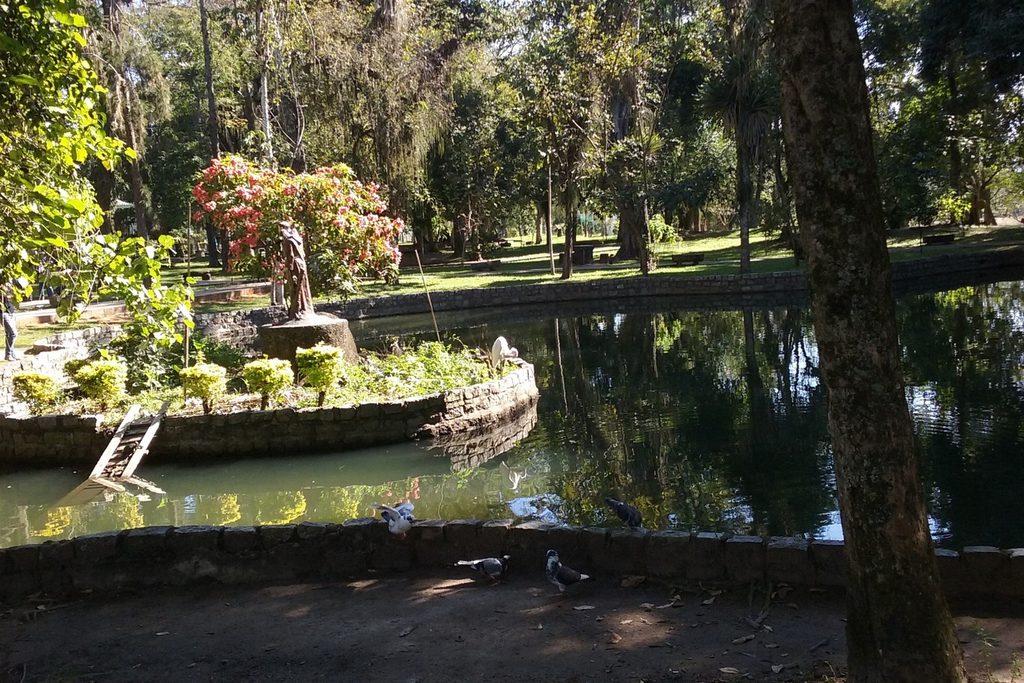 Lago com estátua e jardim entre árvores altas e sombreadas no Bosque da Princesa, em Pindamonhangaba
