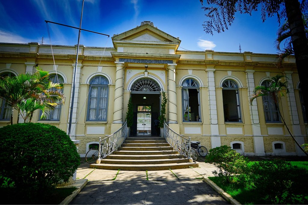 Fachada amarela com colunas, escadaria e janelas em arco do Grupo Escolar Dr. Alfredo Pujol, no centro de Pindamonhangaba