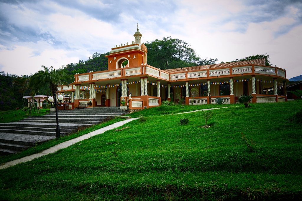 Templo laranja e branco da Fazenda Nova Gokula no alto de um gramado, com escadaria e a mata da Mantiqueira ao fundo