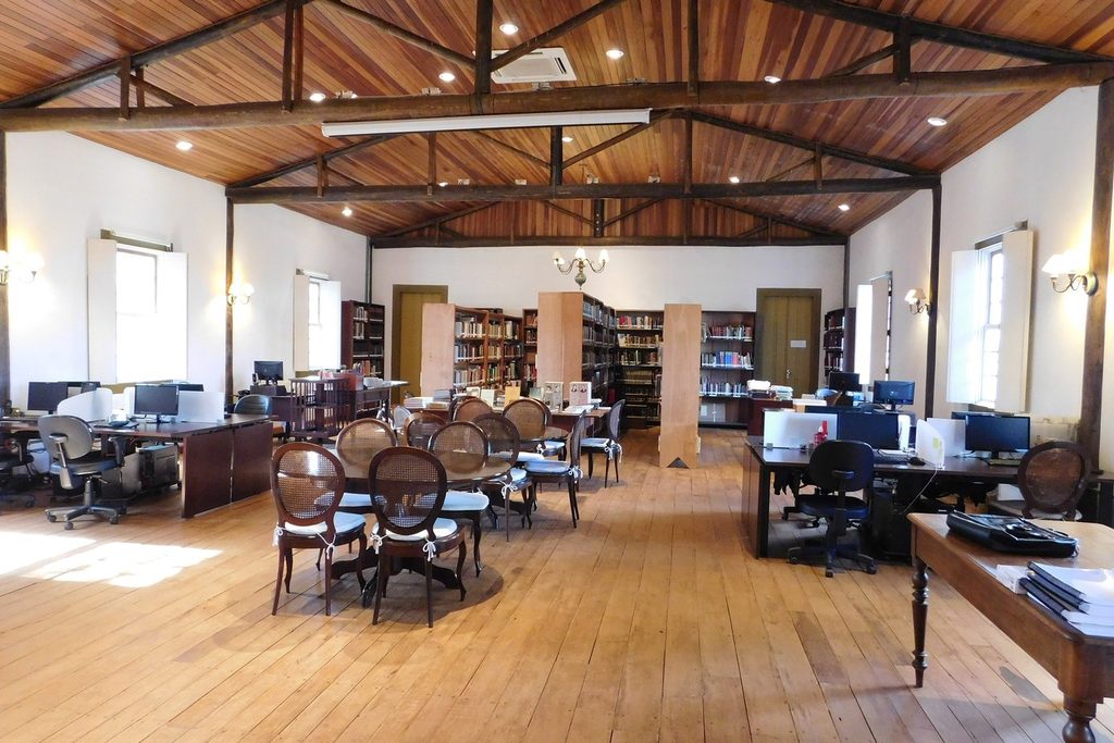 Sala ampla com forro de madeira, estantes de livros, mesas e cadeiras do centro de estudos da Fazenda do Pinhal