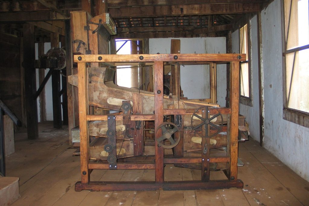 Máquina antiga de madeira com engrenagens de ferro usada no beneficiamento do café, num galpão de assoalho de madeira