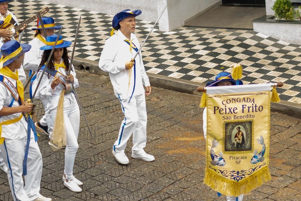 Grupo de congada de Piracaia vestido de branco e azul, com chapéus e o estandarte da Congada Peixe Frito