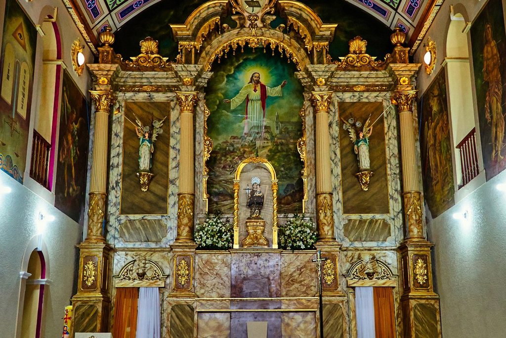 Altar dourado e ornamentado da Igreja Nossa Senhora do Rosário, com imagens de santos e pintura de Cristo