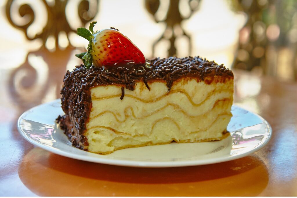 Fatia de torta Napoleão de Piraju com camadas de massa e creme, cobertura de chocolate com granulado e um morango no topo