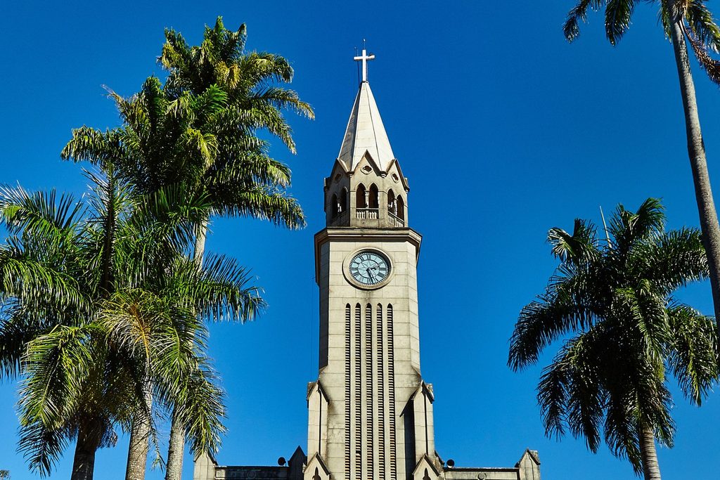Igreja Matriz de São Sebastião de Piraju, em estilo gótico, com torre do relógio e palmeiras altas sob céu azul