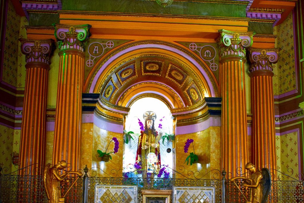 Altar dourado e colorido com colunas e arco, com a imagem do Senhor Bom Jesus ao centro, cercada de flores