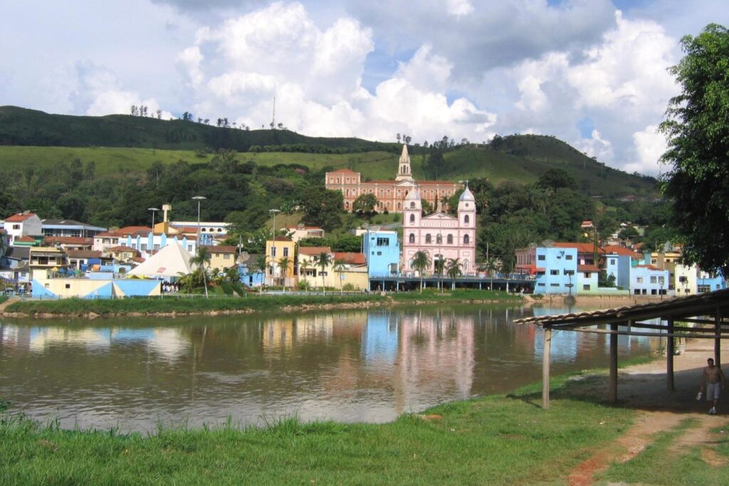 Casas coloridas e igrejas de Pirapora do Bom Jesus refletidas no rio, com morros verdes ao fundo