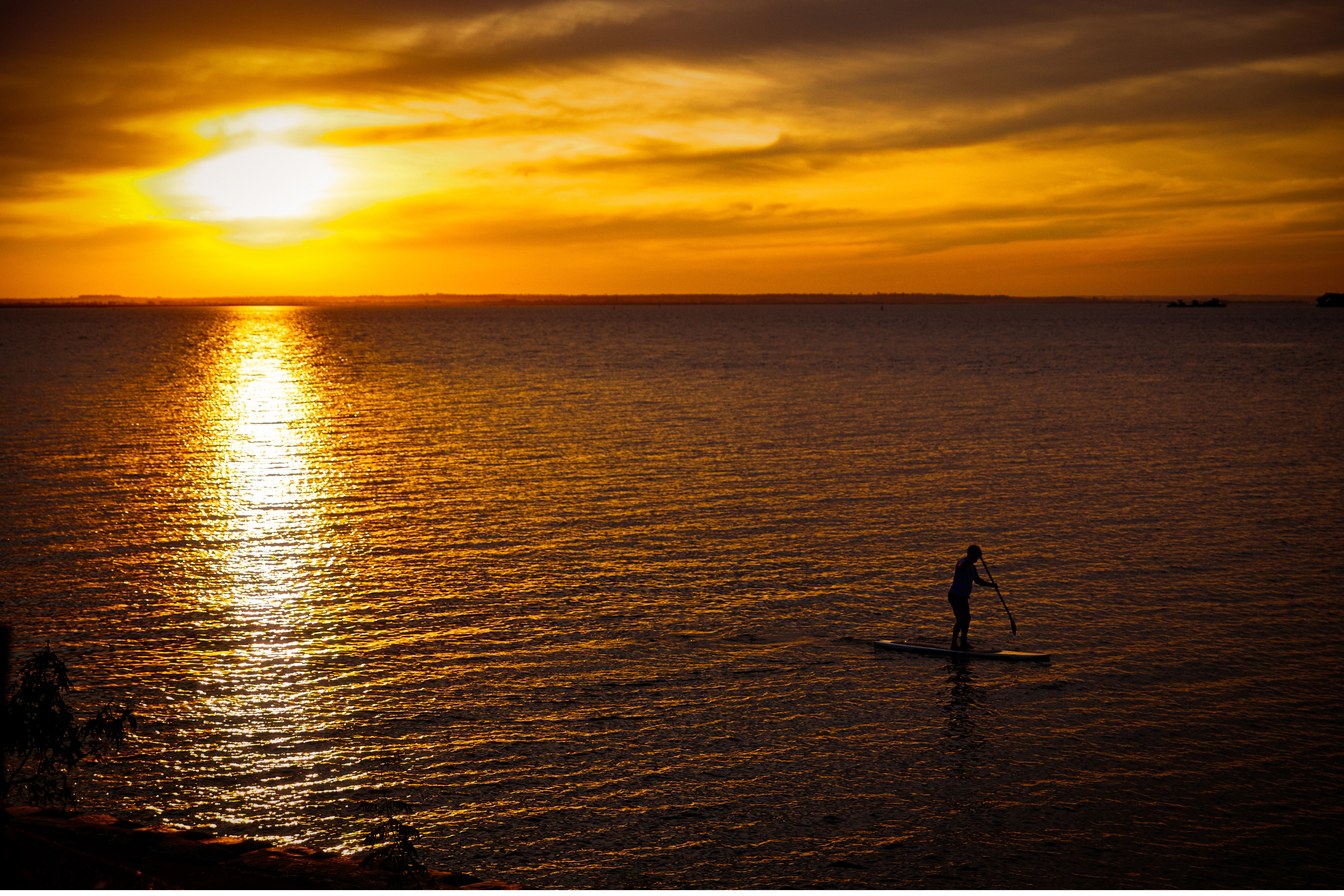 Pôr do sol dourado sobre o Rio Paraná em Presidente Epitácio, com a silhueta de uma pessoa remando de stand-up