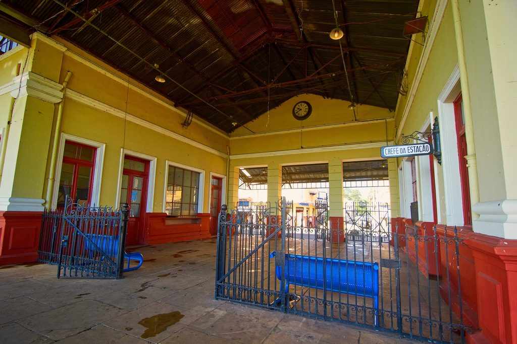 Plataforma coberta da antiga estação ferroviária de Rio Claro, com paredes amarelas, portas vermelhas, relógio e placa de chefe da estação