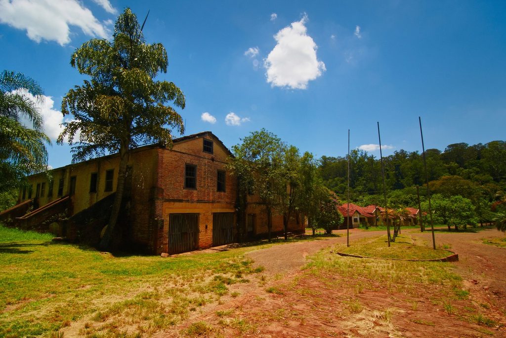 Antigo galpão de tijolos de dois andares e casas de telhado vermelho entre árvores e gramado, na Floresta Estadual de Rio Claro