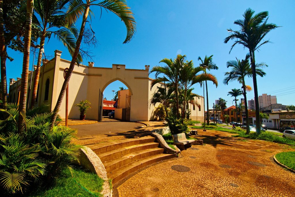 Entrada em arco do Mercado Municipal de Rio Claro, com fachada clara, palmeiras e escadaria de pedra na frente