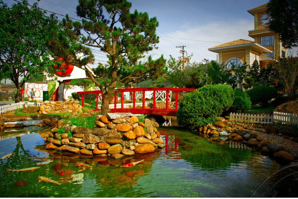 Jardim Oriental de Ribeirão Pires com lago de carpas, pedras, pinheiro e ponte vermelha em estilo japonês