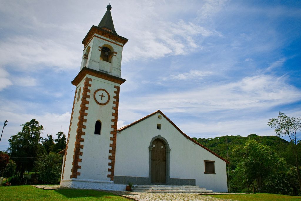 Capela de Nossa Senhora do Pilar, em Ribeirão Pires, branca com torre de cantos marrons e mata ao fundo