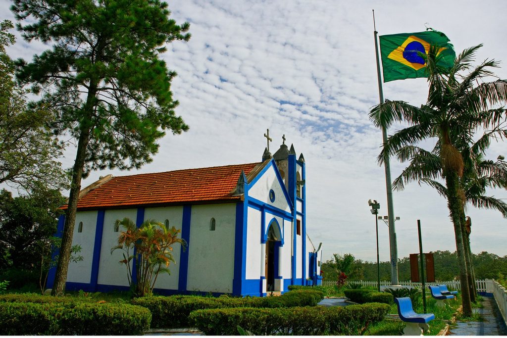 Capela branca e azul do Mirante Santo Antônio, com jardim, palmeiras e bandeira do Brasil