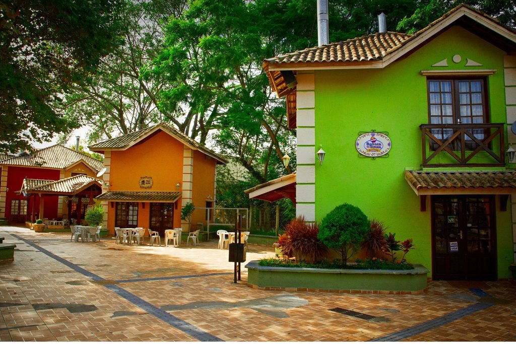 Casinhas coloridas de telhado de barro na Vila do Doce, em Ribeirão Pires, com mesas na calçada