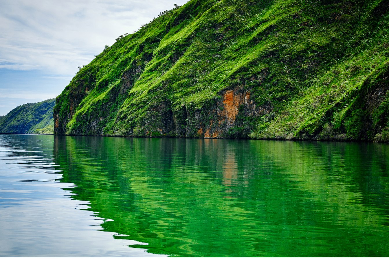 Paredão do Estreito, em Rifaina, encosta de pedra coberta de vegetação verde refletida na água calma do Rio Grande
