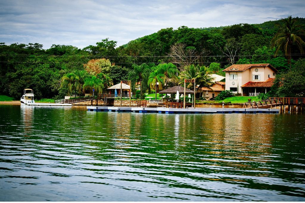 Ranchos de veraneio à beira do lago, com píer, lancha atracada e casa entre palmeiras