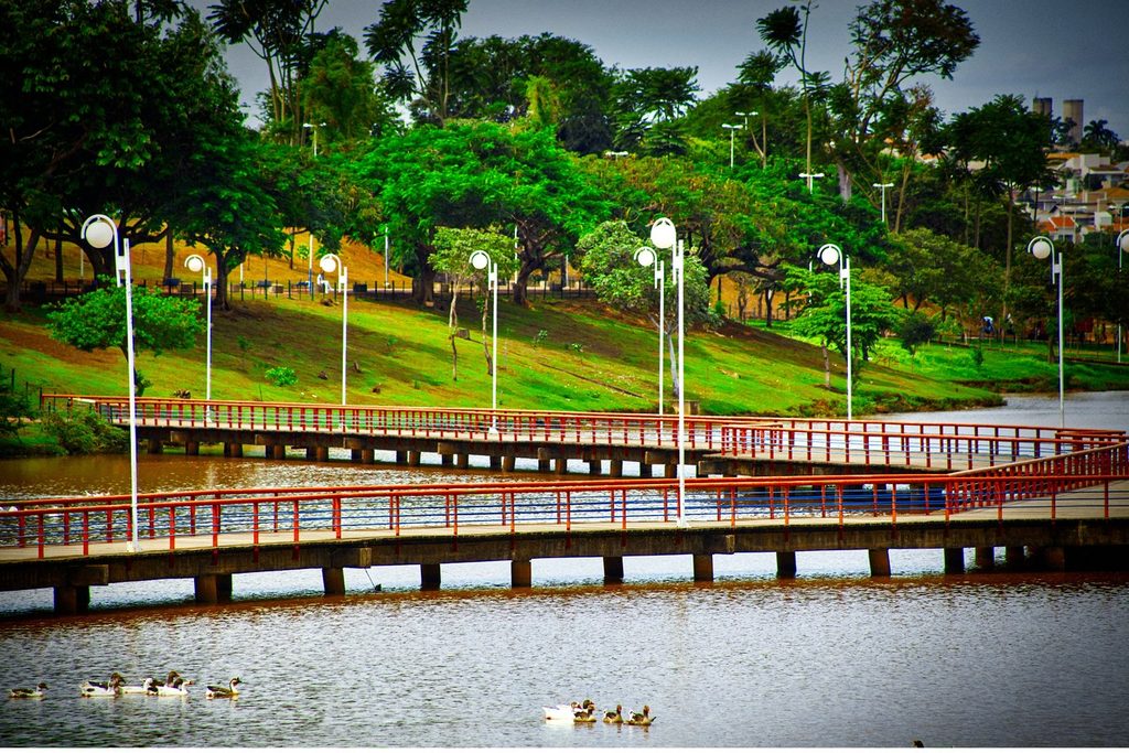 Passarelas de grade vermelha sobre o lago do Parque da Represa Municipal, com patos na água