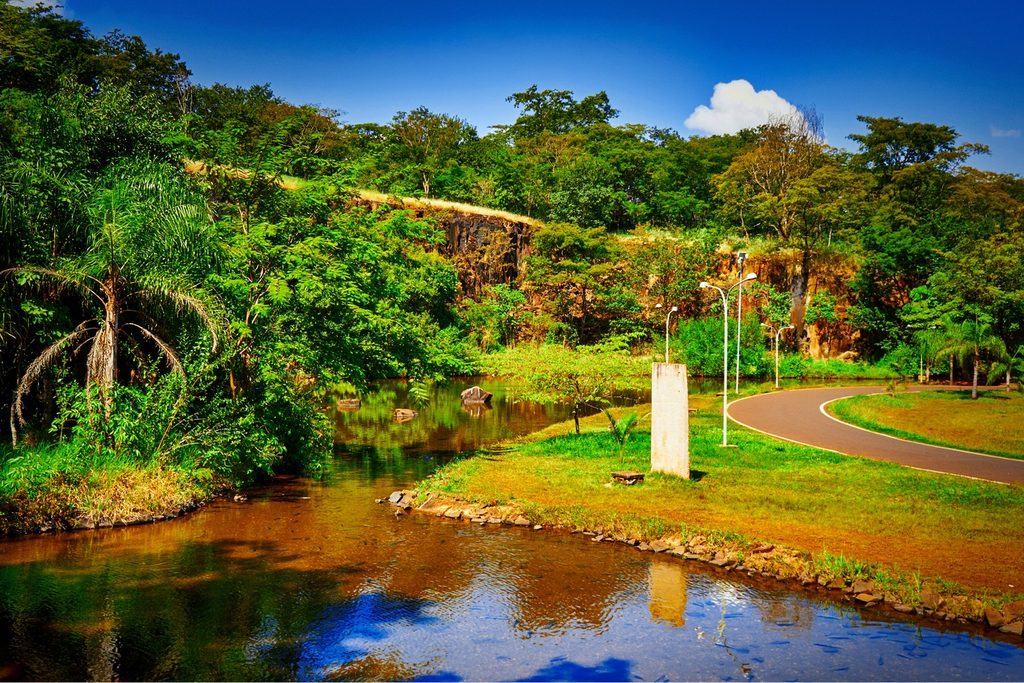 Lago cercado de mata e paredão de pedra da antiga pedreira, com ciclovia, no Parque Curupira, em Ribeirão Preto