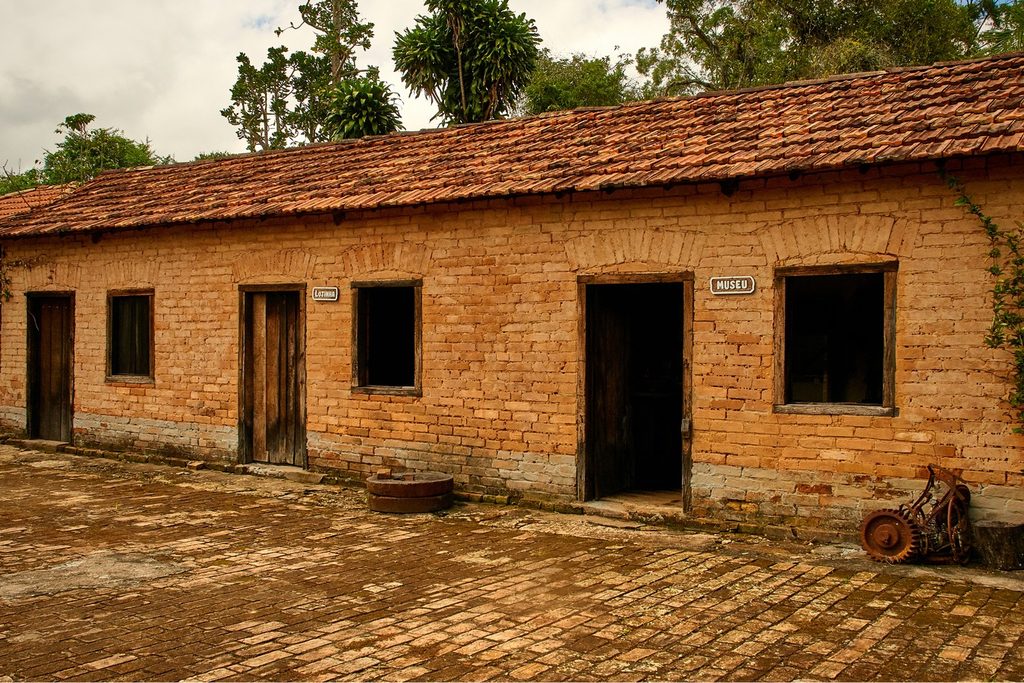 Construção antiga de tijolos aparentes e telhado colonial no Casarão do Café, com pátio de tijolos e peças antigas na frente