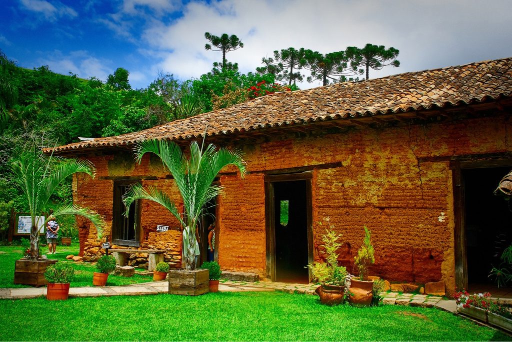 Casarão de taipa com telhado de barro e jardim florido com vasos, no restaurante Casarão Senzala, em Salesópolis