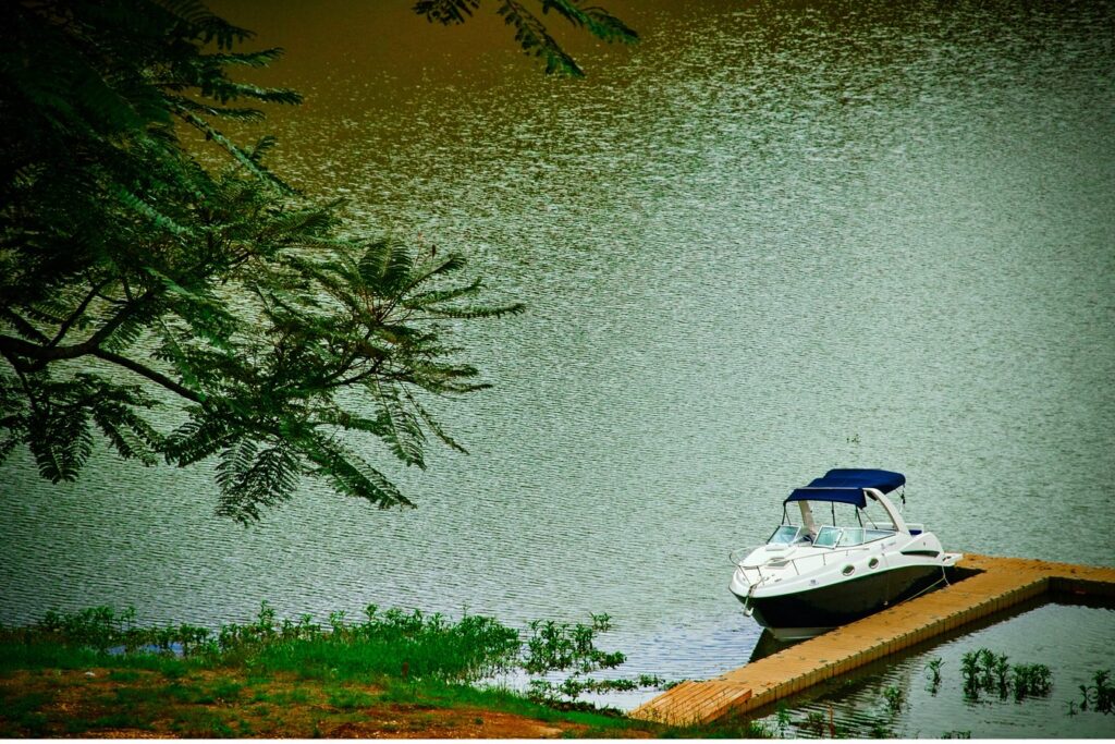 Lancha branca parada num deque de madeira na Represa do Jaguari, em Santa Isabel, com galhos de árvore em primeiro plano