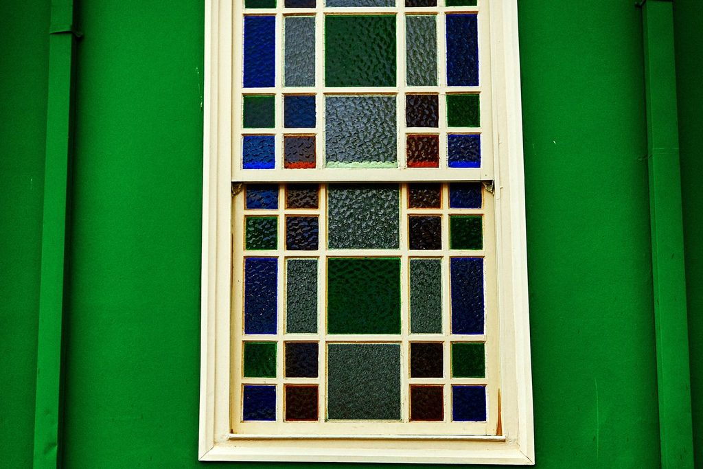Janela antiga de madeira com vidros coloridos azuis e verdes numa parede verde