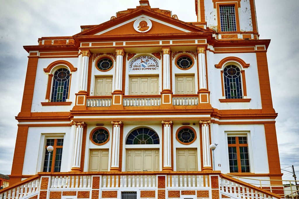 Fachada branca e laranja do Mosteiro Cisterciense de Nossa Senhora de São Bernardo, com janelas em arco e colunas