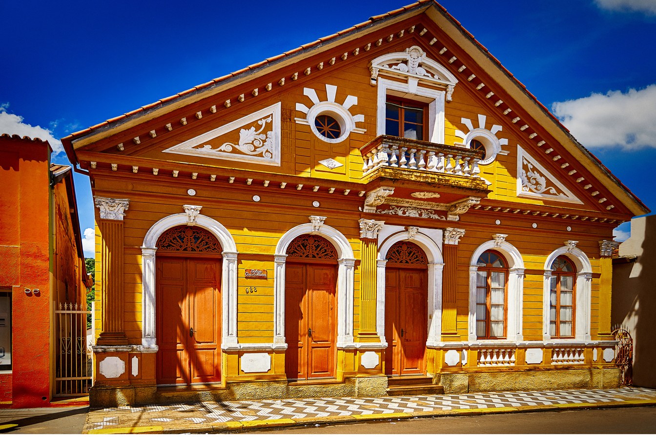 Casarão amarelo com detalhes brancos, portas de madeira e frontão decorado no centro histórico de São Simão SP