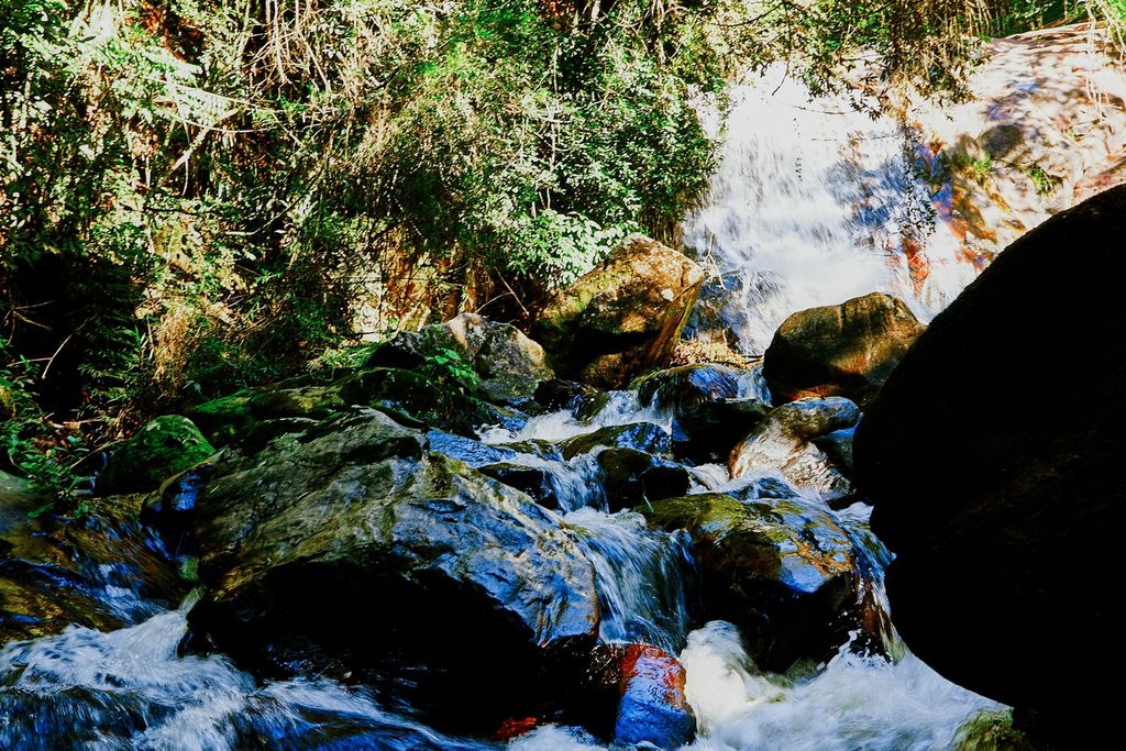 Cachoeira descendo entre pedras grandes e mata, formando corredeiras de água branca, na Cachoeira do Lageado