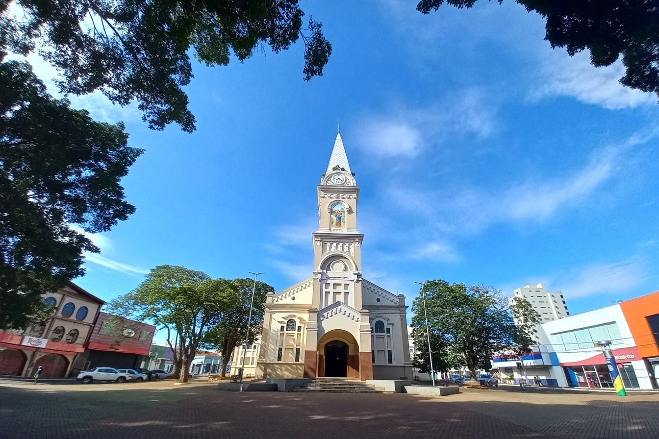 Igreja Matriz de Santa Bárbara d'Oeste, clara, com torre do relógio pontiaguda, vista da praça central sob céu azul
