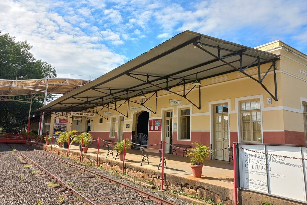 Antiga estação ferroviária de Santa Bárbara d'Oeste, amarela, com plataforma coberta e trilhos em primeiro plano