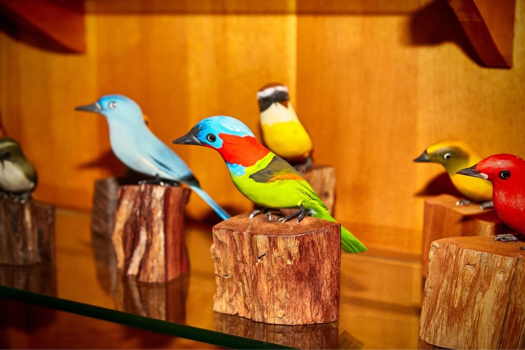 Pássaros de madeira pintados à mão em cores vivas, pousados sobre tocos, no artesanato de Silveiras