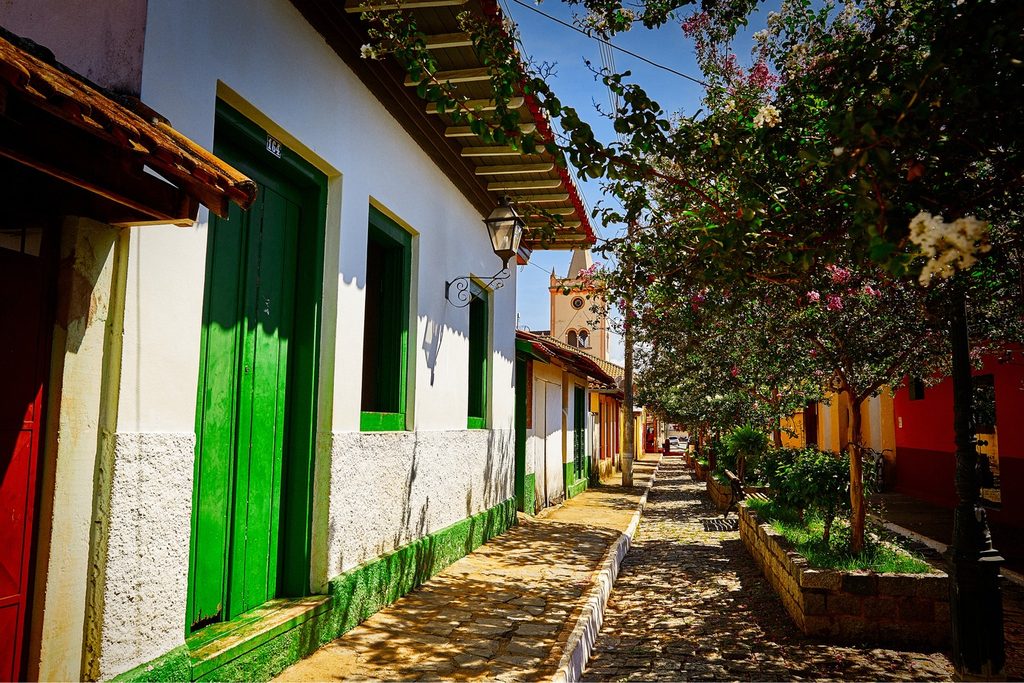 Rua de pedras com casas coloniais brancas de portas verdes e a torre da igreja ao fundo, no centro histórico de Silveiras