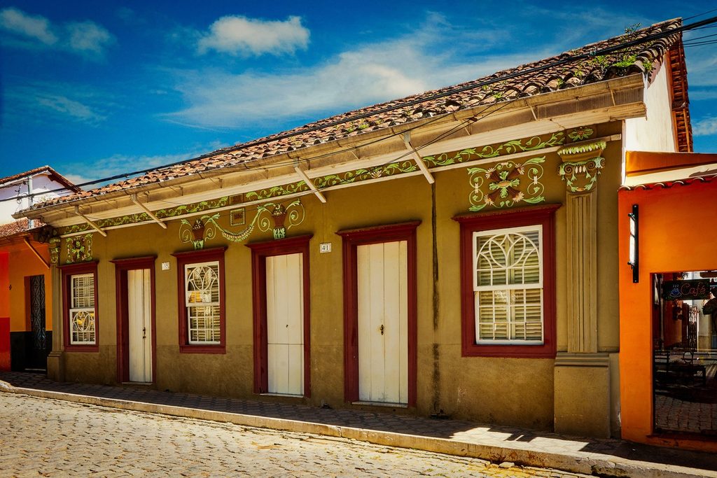 Casarão colonial com portas e janelas vermelhas e ornamentos coloridos na fachada, numa rua de paralelepípedos do centro de São José do Barreiro