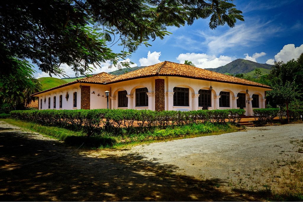 Casarão térreo em estilo espanhol com arcos e telhado de telhas do Clube dos 200, entre jardim e morros