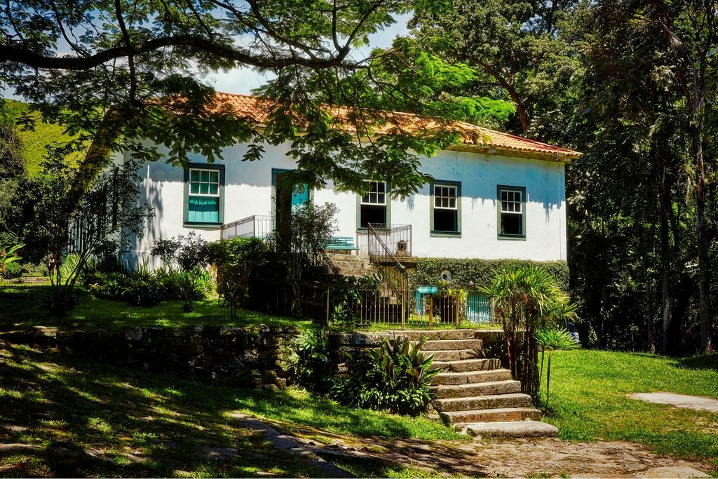 Casa-sede branca da Fazenda da Barra, em São José do Barreiro, com janelas verdes, escada de pedra e jardim sob árvores grandes
