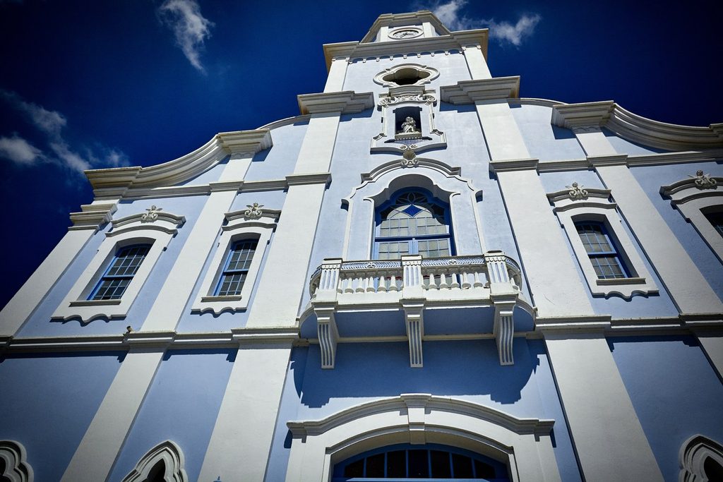Fachada azul-clara e branca da Igreja Matriz de São José, vista de baixo contra o céu azul